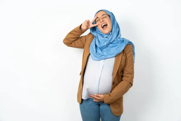 妊娠したイスラム教徒の女性は 顔に指で平和のシンボルを行い 陽気な笑顔で勝利を示しています — ストック写真