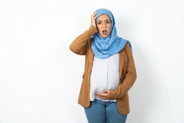 衝撃的な表情でヒジャーブを着用している恥ずかしい妊娠中のイスラム教徒の女性は素晴らしい驚きを表現し パズルされた少女は屋内でポーズします — ストック写真