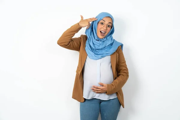 美しい妊娠したイスラム教徒の女性は 指で寺院のショットの周りにヒジャーブ愚かさを着用して自殺のジェスチャーを作ります 面白い ガール ピストル — ストック写真