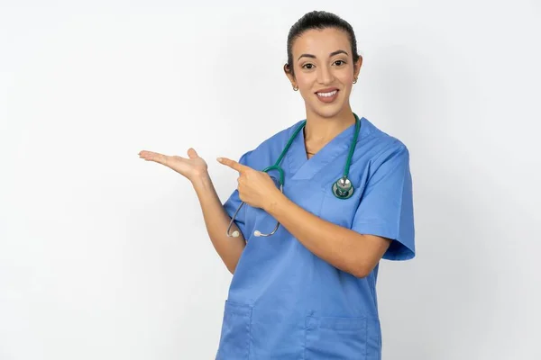 青い制服のプロモーターポイント指のコピースペースを身に着けている肯定的なアラブの医師の女性は手を握ります提供の広告のプロモーションを示します — ストック写真