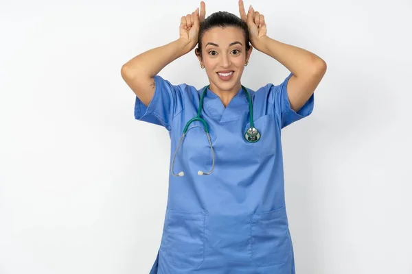 面白いアラブの医師 青い制服を着ている女性は角を示しています 頭のジェスチャーに指 愚かでかわいいポーズ — ストック写真