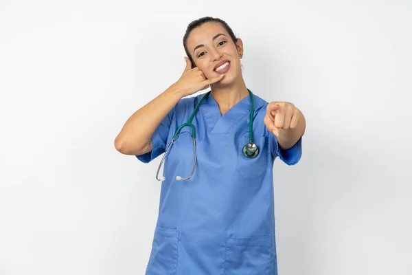 アラブの医師の女性 青い制服を着て笑顔で 後でジェスチャーをかけながらカメラを指差し 電話で話す — ストック写真