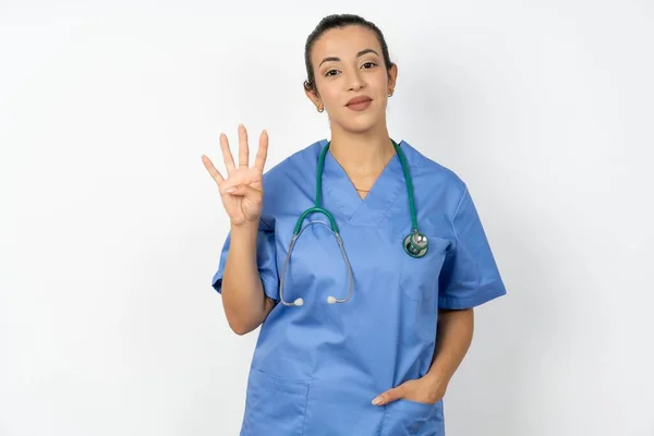 アラブの医師の女性は青い制服を着て自信を持って幸せに微笑んでいる間指番号4を指で指を指さす — ストック写真