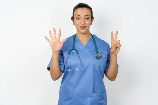 アラブの医師の女性は青い制服を着て自信と幸せに微笑んでいる間指番号7を指で指で指を指さす — ストック写真