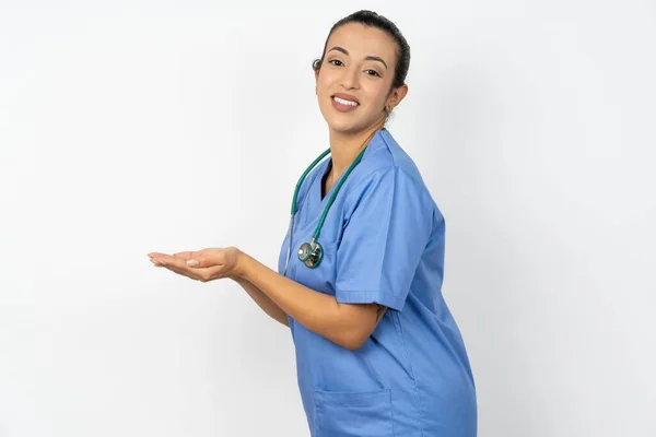 アラブの医師の女性は コピースペースを示す手の開いた手のひらの脇に青い制服を着て 興奮する笑顔の広告を提示します — ストック写真