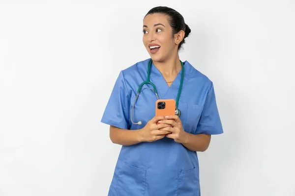 アラブの医師の女性は スマートフォンを保持し 空白のコピースペースで側面を見ている青い制服を着ています — ストック写真