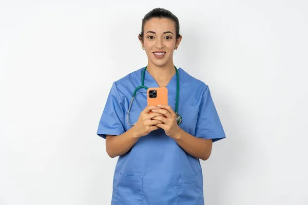 穿着蓝色制服的医生女士喜欢远距离交流 使用手机 在网上飞速冲浪 笑得愉快 在网上购物 — 图库照片