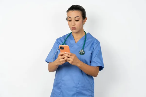 エキサイティングなアラブの医師の女性は 青い制服ウィンキングとアイホールドスマートフォン使用読み取りソーシャルネットワークニュース — ストック写真
