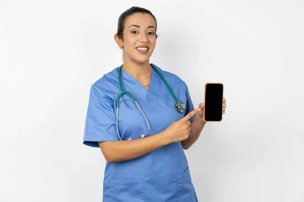 迷人的快乐的阿拉伯医生女士 身穿蓝色制服 手持显示黑色屏幕的手机 — 图库照片