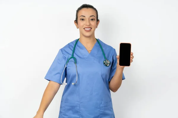 穿着蓝色制服微笑的阿拉伯医生女人拿着空白屏幕的手机 — 图库照片