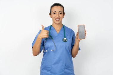 Mavi üniforma giyen Arap doktor kadın boş ekran akıllı telefonu göster, başparmağını kaldır ve yeni bir uygulama tavsiye et