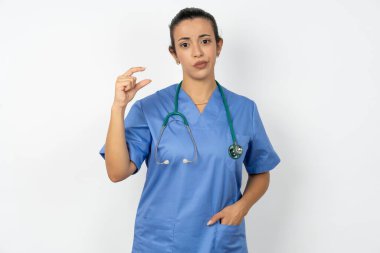 Mavi üniforma giyen hoşnutsuz Arap doktor kadın küçük el işaretleri çok büyük olmayan bir şeyi gösteriyor. Vücut dili kavramı.