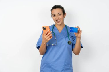 Mavi üniformalı Arap doktor kadının elinde modern cep telefonu ve kredi kartı var.