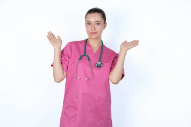 Kafası karışmış, pembe üniformalı, steteskop takmış, omuzlarını silkmiş, 