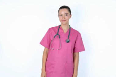 Pembe üniformalı mutlu beyaz kadın doktor. Steteskopla kameraya bakıyor. Sevimli bir gülümsemesi var..