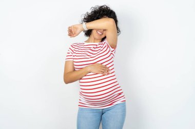 Hamile kadın kollarıyla gözlerini kapatıyor neşeli ve komik gülümsüyor. Kör kavram.