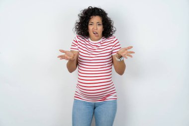 Hüsrana uğramış hamile kadın şaşkın ve tereddütlü hissediyor, şaşkınlıkla omuz silkiyor, ağzını açık tutuyor, ne yapacağını bilmiyor..