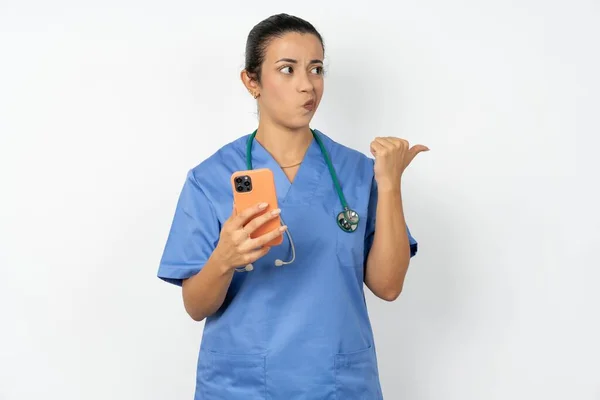 穿着蓝色制服的医生女士把手指移开 把空白处放在一边 拿着手机发短信 — 图库照片