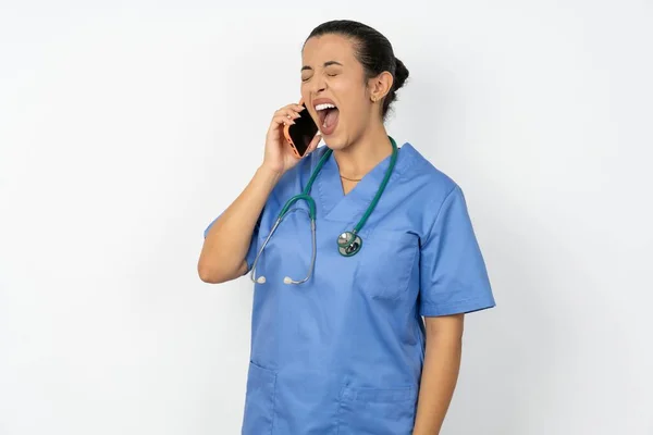 ブルーユニフォームを着ているオーバーメイドのアラブの医師女性は 電話会話中に友人からの面白い話を積極的に聞きます — ストック写真