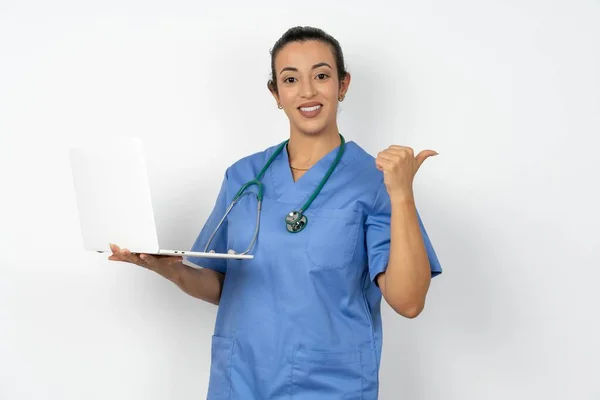 空のスペースを指示する青い制服を着ているアラブの医師の女性はラップトップを保持します — ストック写真