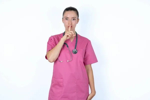 stock image caucasian woman doctor in pink uniform with stethoscope makes hush gesture, asks be quiet. Don't tell my secret or not speak too loud, please!