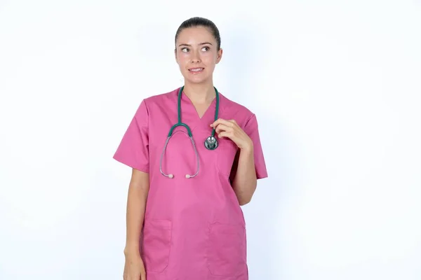 おっと オプス ステスコープでピンクのユニフォームの白人女性医師の肖像画は 混乱して脇に見える 彼女の悪い間違いを実現 — ストック写真