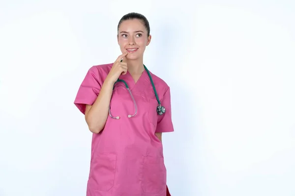 Kaukaska Kobieta Lekarz Różowym Mundurze Stetoskopem Przemyślanym Wyrazem Twarzy Patrzy — Zdjęcie stockowe
