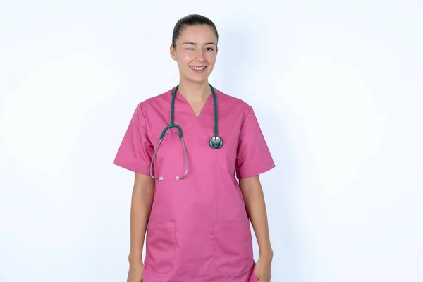白人女性医師 ピンクの制服を着て 目が点滅し 幸せな表情をしています フェイシャル表現と人々の感情コンセプト — ストック写真
