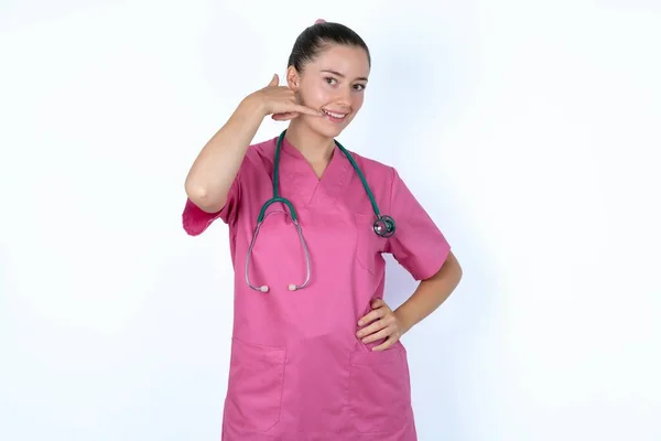 ピンクの制服の白人女性医師は 電話の会話を模倣し 手で電話のジェスチャーを作り 自信を持って表現しています 電話する — ストック写真