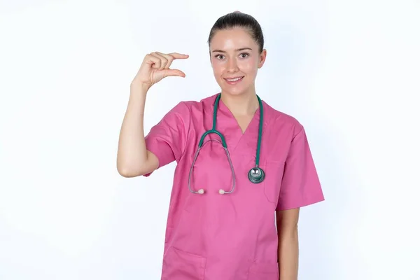 手の小さなサイズの笑顔とジェスチャーでピンクのユニフォームの白人女性医師 測定シンボル — ストック写真
