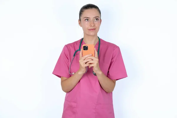 スマートフォンを保持しながら 夢のような外観を持つ白人女性医師の肖像画 メッセージを書くために試みる — ストック写真