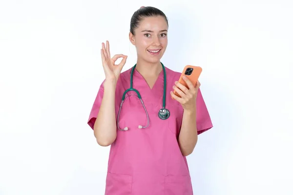 快乐的高加索女医生用他的智能手机发送一个信息 或者拿着一个自拍照 然后用手签个名 — 图库照片