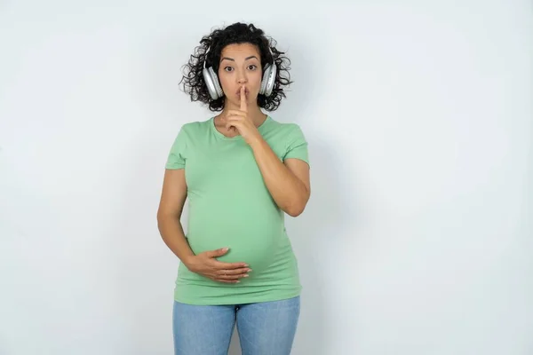 孕妇戴着无线耳机 用手指捂住嘴唇 做着一个沉默的手势 安静点 — 图库照片