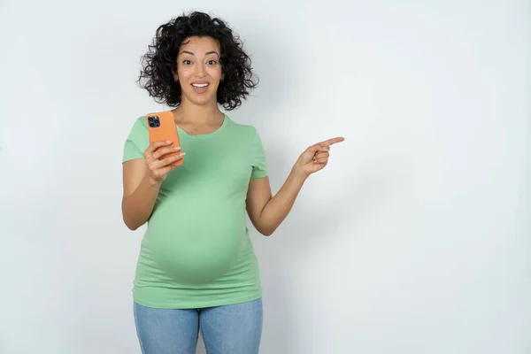 Astonished Pregnant Woman Holding Her Telephone Pointing Finger Aside Empty — Stock Photo, Image