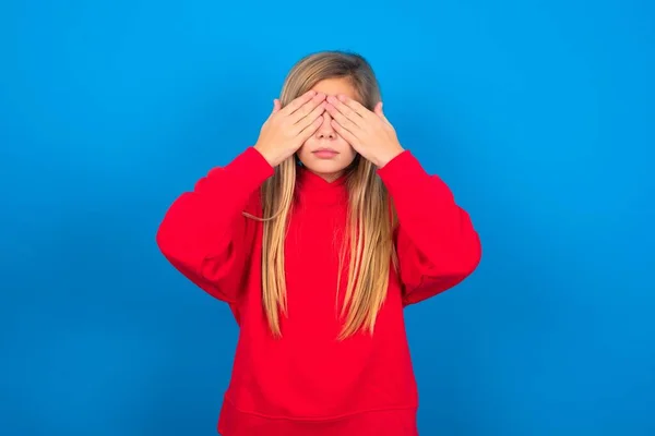 両手で目を覆う青い壁の上に赤いセーターを着ている美しい白人の十代の少女は 何も見たり 恥ずかしいと感じたりしたくありません 人間の感情の反応 — ストック写真