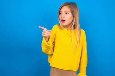 Mavi duvarda sarı süveter giyen, afallamış sarışın genç kız fotokopi alanının ötesini işaret ediyor.