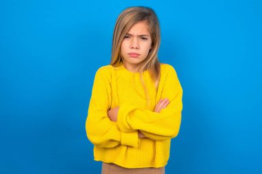Mavi duvarda sarı süveter giyen güzel sarışın kız parmaklarını göstererek reklamını yapıyor, şaşırmış yüzünü ve ağzını açıyor.