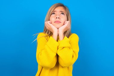 Mavi duvarın üzerine sarı kazak giyen üzgün sarışın genç kızın portresi boş görünüyor.