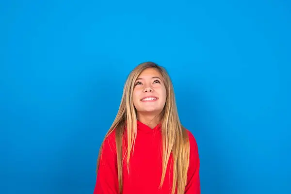 謎の笑顔を見上げる青い壁の上に赤いセーターを着ている神秘的な美しい白人十代の少女の肖像画 広告コンセプト — ストック写真