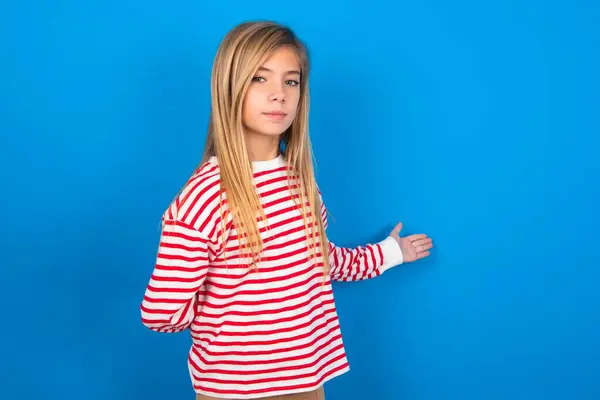 美しい白人十代の少女の肖像画は 歓迎するジェスチャーでアームアウト青いスタジオの背景にストライプシャツを着用 — ストック写真