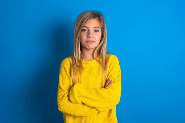 自信を持って深刻な落ち着いた美しいブロンドの十代の少女は 青い壁の上に黄色のセーターを着用し 腕を折りました プロの雰囲気は主張的なポーズで立っています — ストック写真