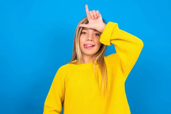 美しいブロンドの十代の少女は額に指で黄色いセーターを着用し 敗者のジェスチャーは人々の舌を示す楽しいを作ります — ストック写真