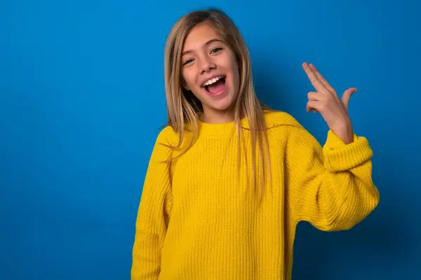 美しいブロンドの十代の少女は 指で寺院でのショットの周りの青い壁の愚かさの上に黄色のセーターを着用して自殺のジェスチャーを作ります おかしいモデルは指ガンピストルを作ります — ストック写真