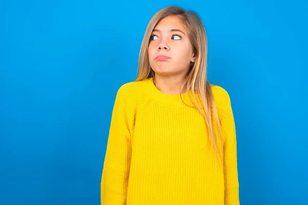 青い壁の上に黄色いセーターを着ている不満の美しいブロンドの十代の少女は唇を追いかけ 不幸な表情を見ると怒っています 抑圧された欲求不満モデル — ストック写真