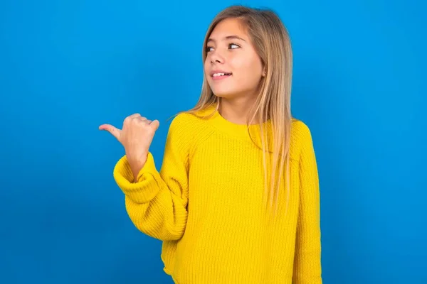 美しいブロンドの十代の少女は青い壁のポイント上の黄色いセーターを身に着け アドバイスは広告を示しています — ストック写真