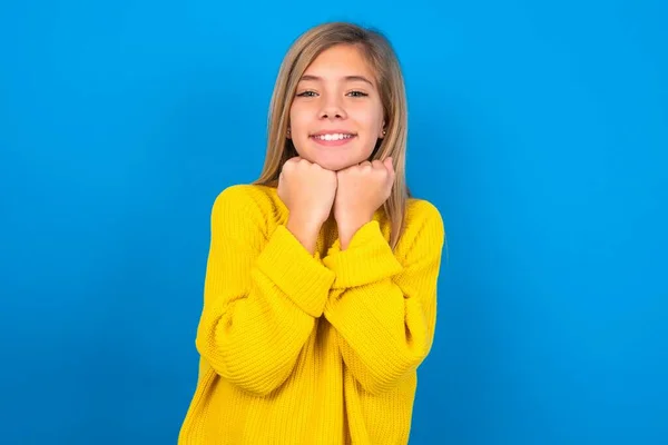 満足した美しいブロンドの十代の少女は青い壁に黄色いセーターを着用し 両手で中国に触れ 快適に微笑み 恋人との良い一日を喜びます — ストック写真