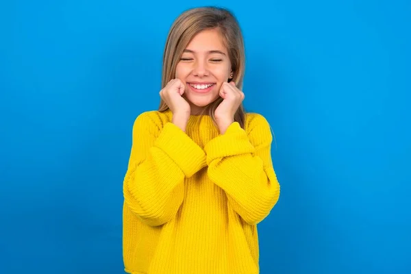美しいブロンドの十代の少女は 青い壁のグリンの上に黄色いセーターを着て喜んで 何か楽しい コピースペースを想像します 楽しい感情コンセプト — ストック写真