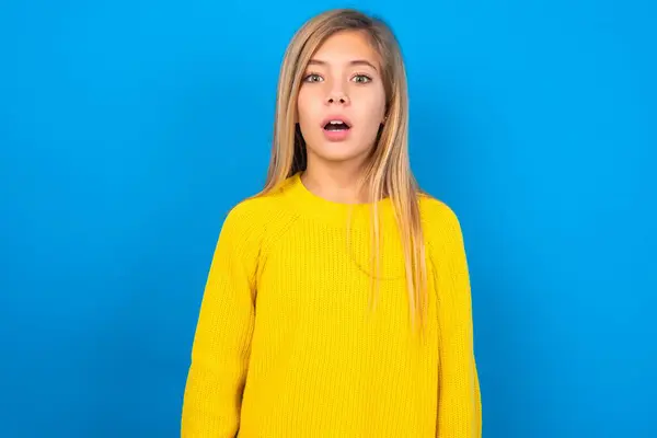 衝撃を受けた美しいブロンドの十代の少女は青い壁の星に黄色いセーターを着用し 虫眼は口を開け続け 驚いた表情をしています Omgコンセプト — ストック写真