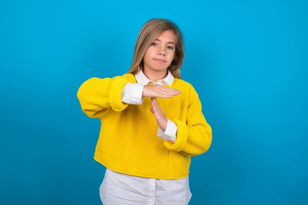 青い壁の上に黄色いセーターを着ている白人の十代の少女はタイムアウトのジェスチャーを示す動揺している 停止する必要があり 懸命な仕事の後の休息のための時間を尋ねます — ストック写真