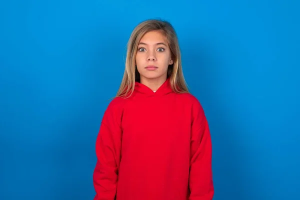 青い壁の星の上に赤いセーターを着用したブロンドの十代の少女は衝撃的なニュースに反応します 驚いた少女は息を止める — ストック写真